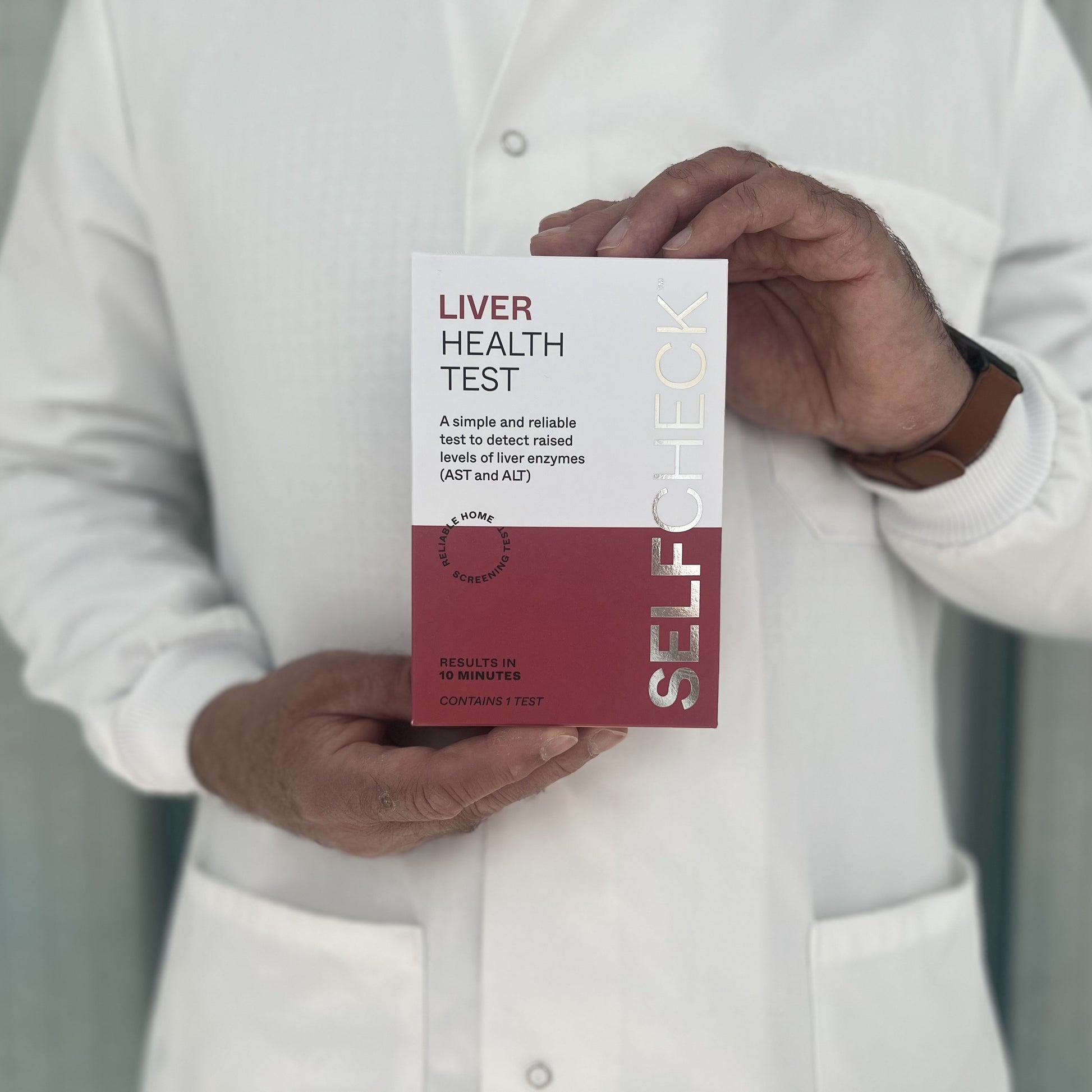 Scientist in white lab coat holding a SELFCHECK Test Kit for Liver Disease