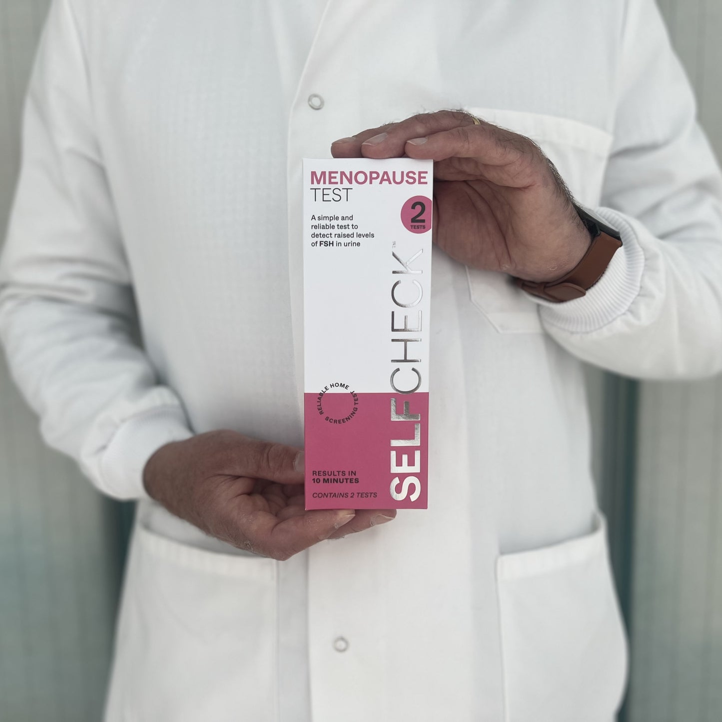 Scientist in white lab coat holding a SELFCHECK Menopause Test Kit