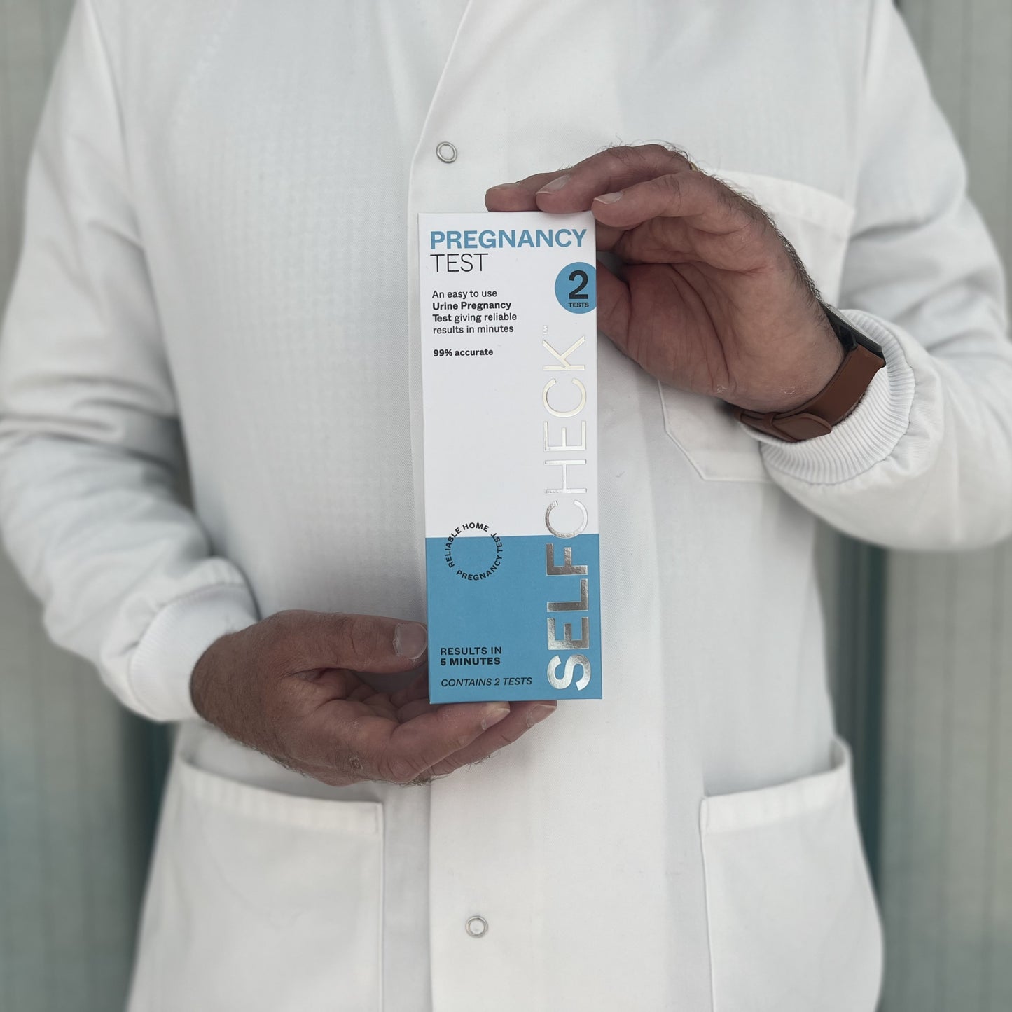 Scientist in white lab coat holding a SELFCHECK Pregnancy Test Kit
