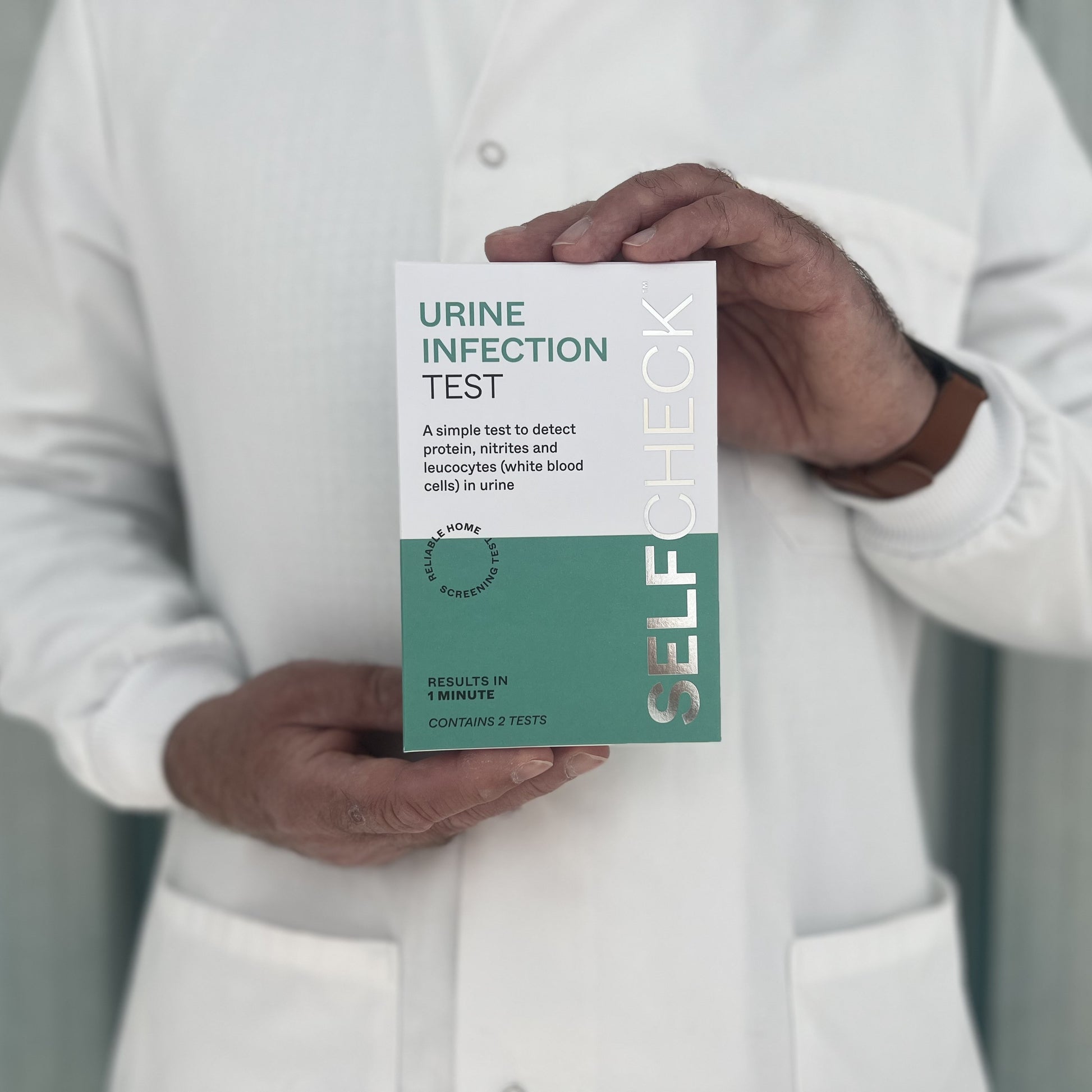 Scientist in white lab coat holding a SELFCHECK Test Kit for urine infections