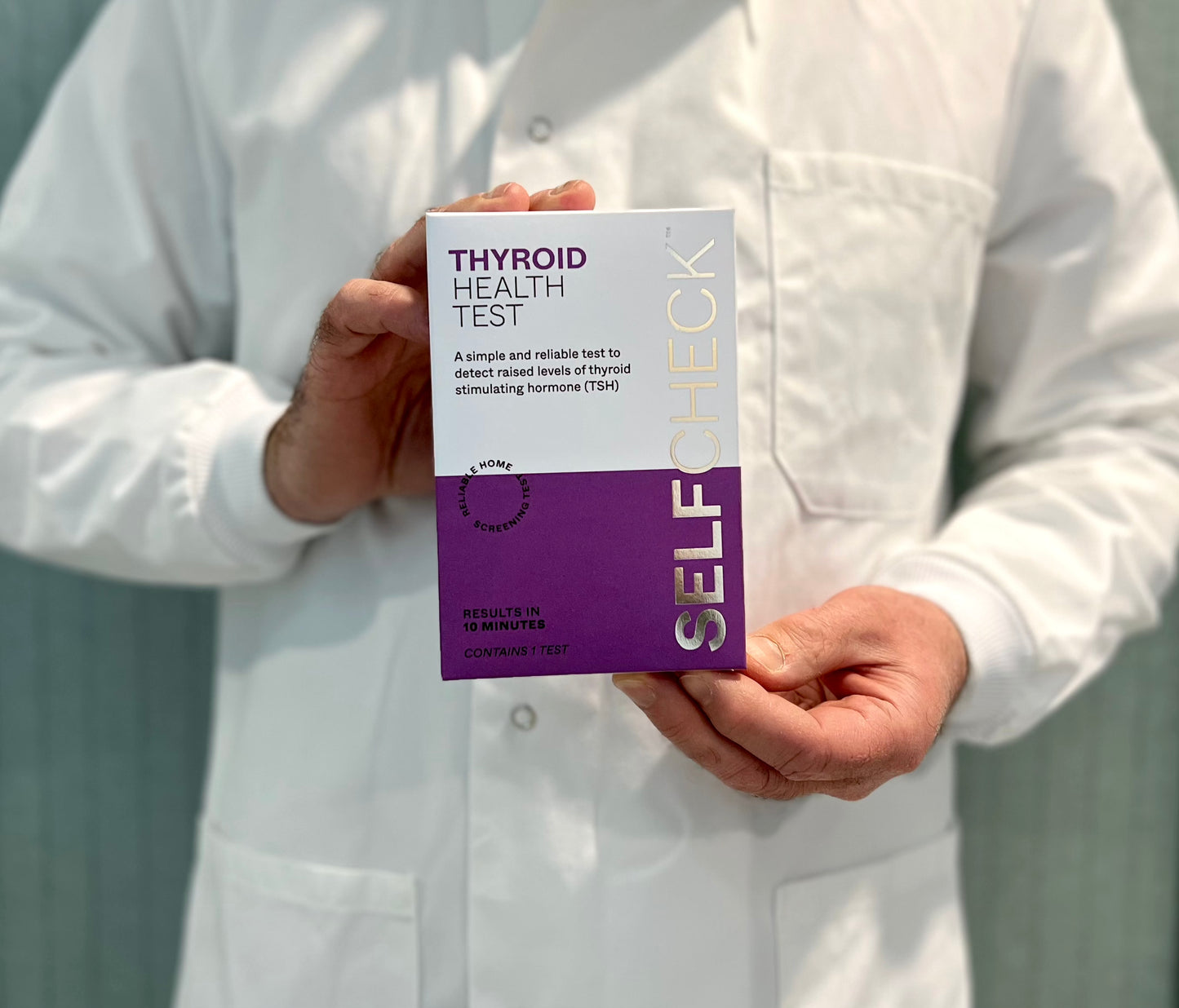 Scientist in lab coat holding SELFCHECK Thyroid Health Test Kit