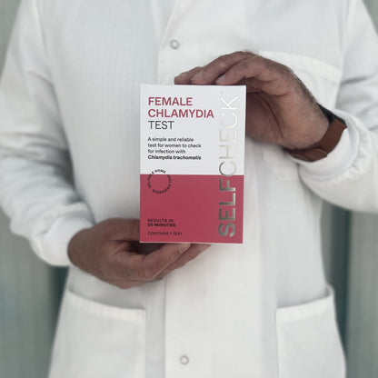 Scientist in white lab coat holding a SELFCHECK Chlamydia Test Kit for women