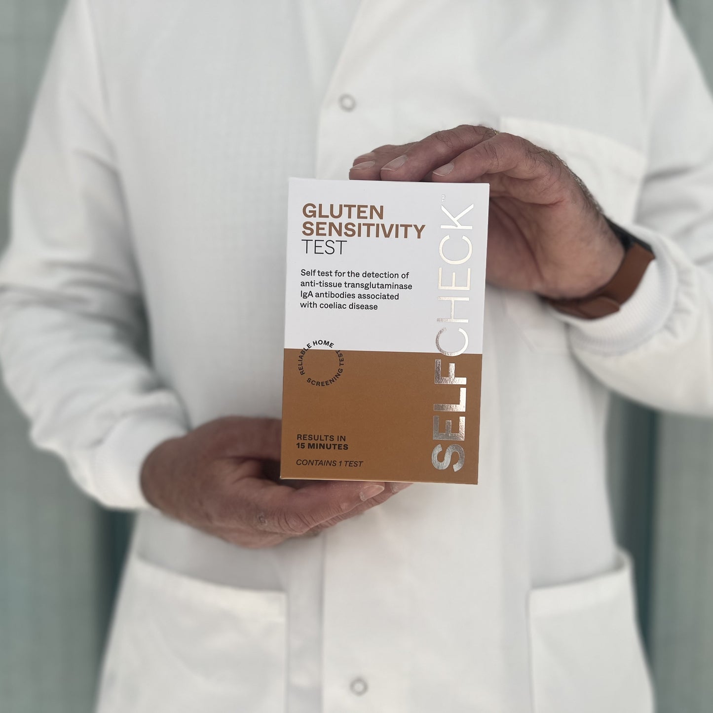 Scientist in white lab coat holding a SELFCHECK Test Kit for coeliac disease