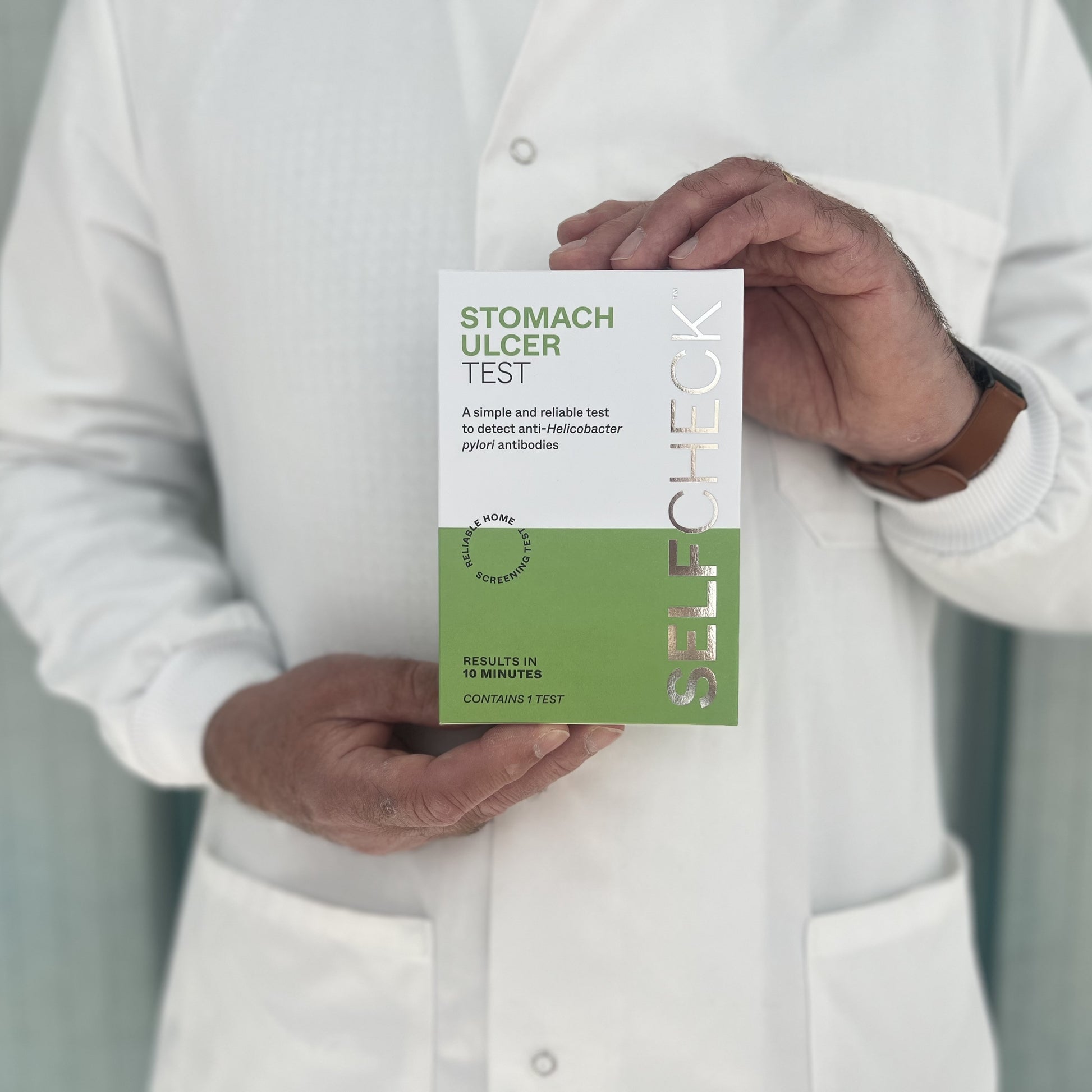 Scientist in white lab coat holding a SELFCHECK Test Kit for stomach ulcers - H pylori antibodies in blood
