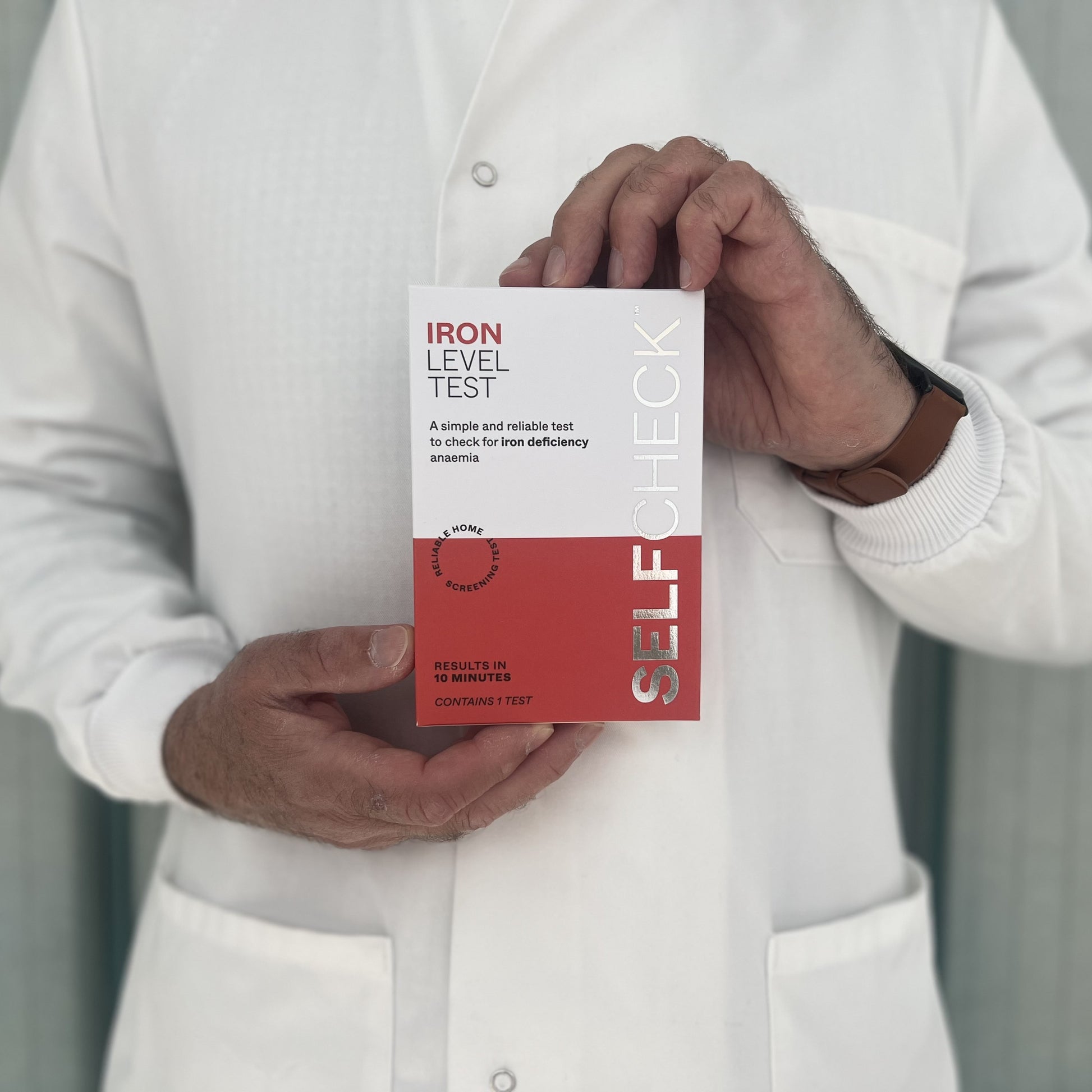 Scientist in white lab coat holding a SELFCHECK Test Kit for Iron Deficiency