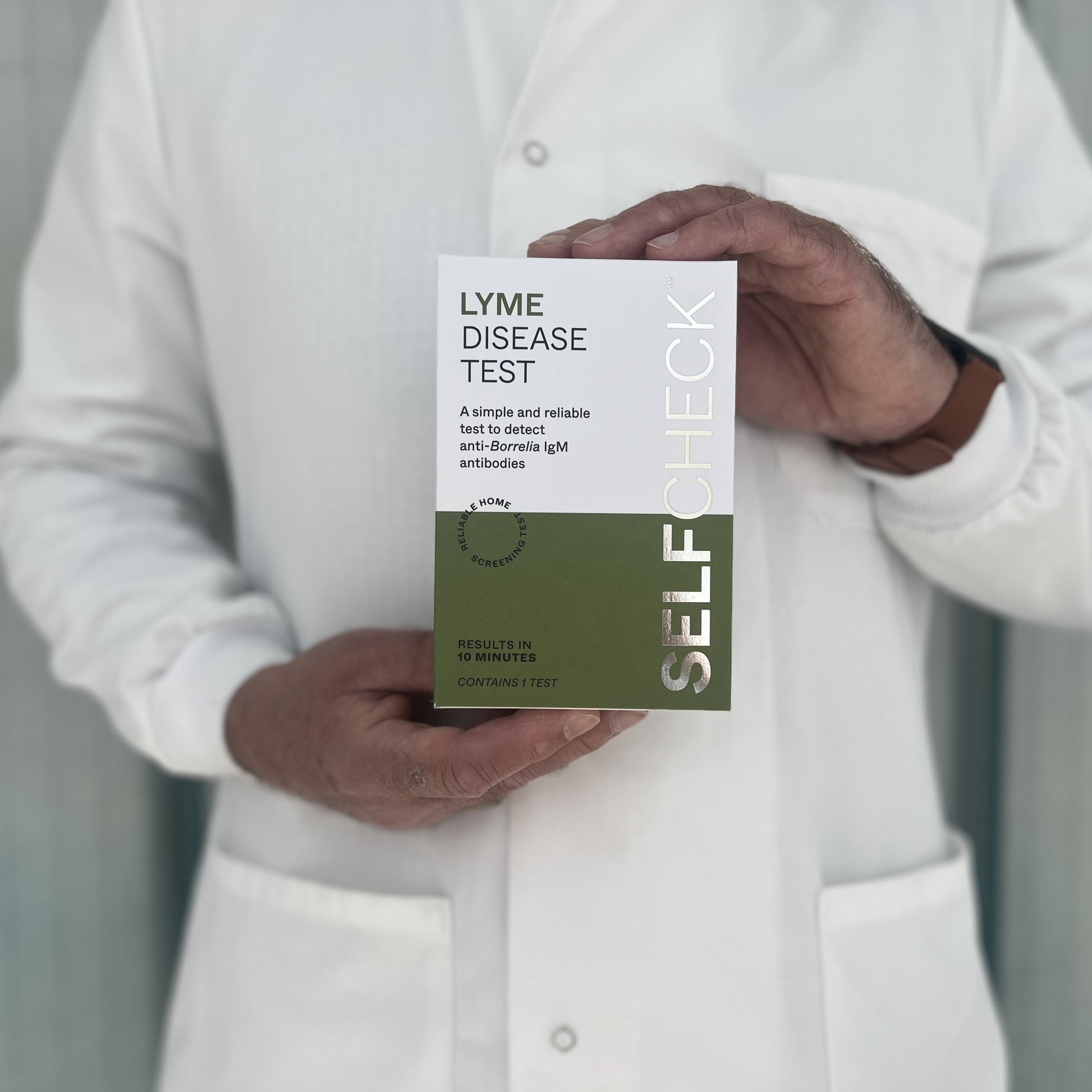 Scientist in white lab coat holding a SELFCHECK Test Kit for Lyme Disease