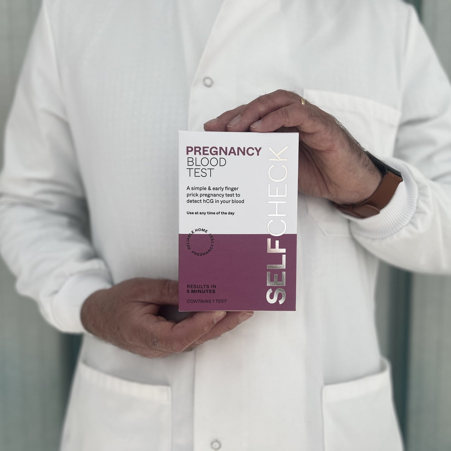 Scientist in white lab coat holding a SELFCHECK Pregnancy Blood Test kit