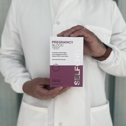 Scientist in white lab coat holding a SELFCHECK Pregnancy Blood Test kit